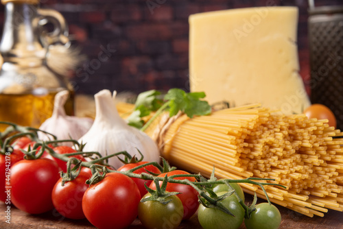 Italian pasta (macaroni), spaghetti tied with sisal string, tomatoes, olive oil, cheese and spices on rustic wood, selective focus.