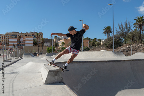 Young skateboarder man does a trick called `Rock to fakie` on the edge of a pool in a skate park. profile view