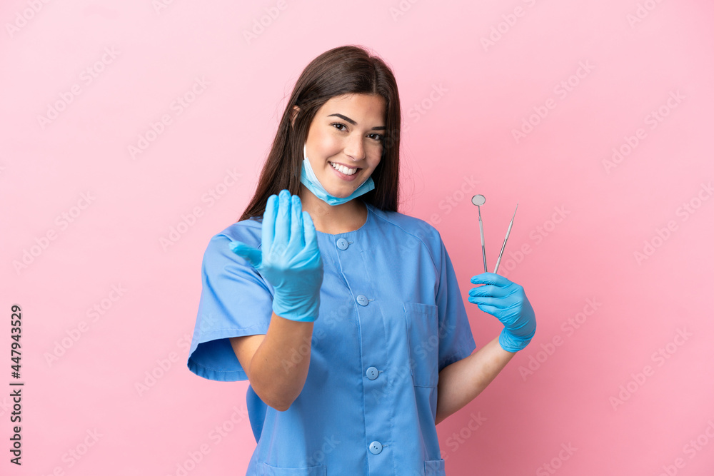 Dentist woman holding tools isolated on pink background inviting to come with hand. Happy that you came - obrazy, fototapety, plakaty 