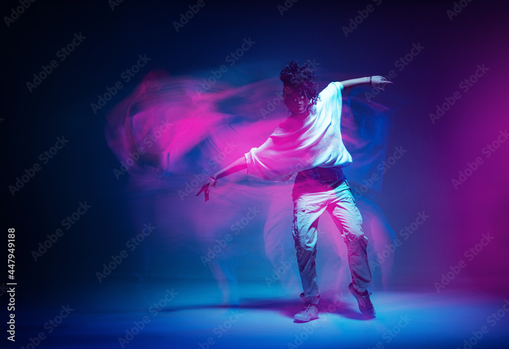 Stylish dancing modern girl moving in colorful neon studio light. Long exposure. Copy space - obrazy, fototapety, plakaty 