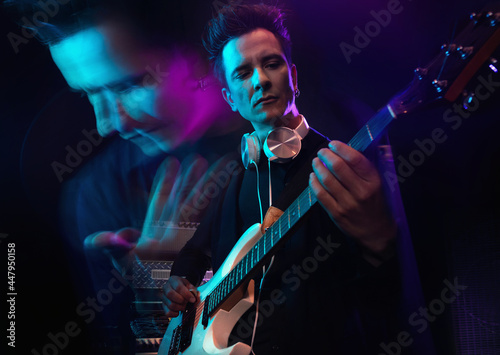 Handsome male musician with electric guitar in recording studio. Guitarist performance. Guitar player strumming. Rock music concept. Multiple exposure neon atmosphere on background.