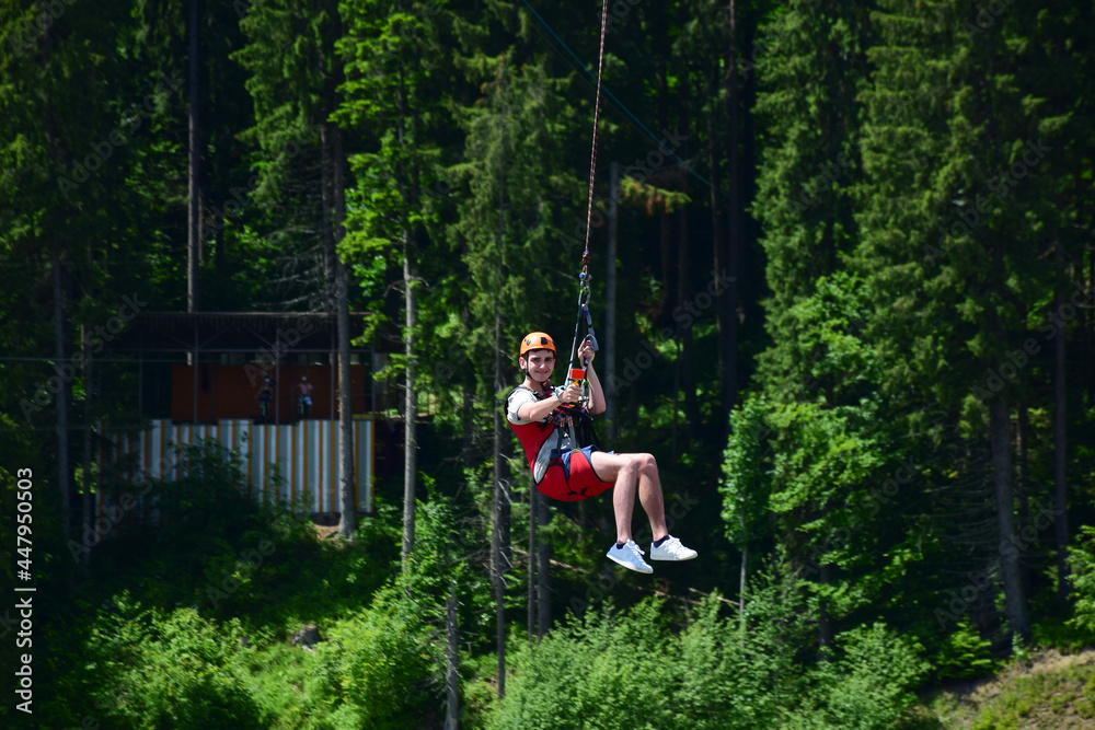 A young man jumped from bungee jumping and now hangs on a rope and films himself on a sports video camera against a blurred background of a green forest