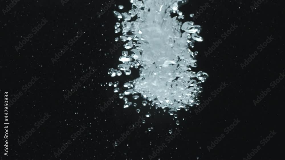 Slowmo close up of air bubbles falling down and flowing upwards in water against dark background