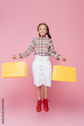 Happy preteen kid with shopping bags levitating isolated on pink