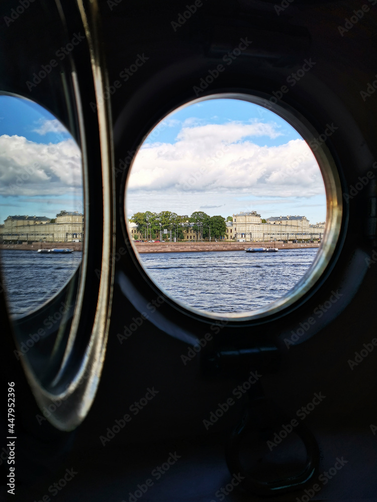 Russia, St. Petersburg - August 2020. View of the Neva and Pirogovskaya embankment through the porthole of the cruiser Aurora.