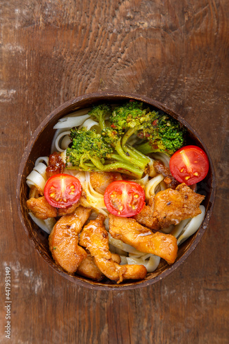 Udon with chicken in Japanese sauce on a plate of coconut shells on a wooden table. Vertical photo