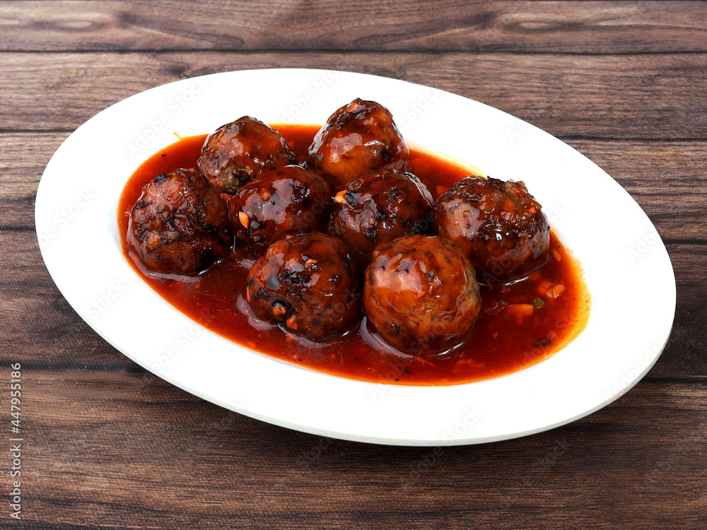 Veg Manchurian, Popular indo-chinese food made of cauliflower florets and other vegetable, served in a white plate over a rustic wooden table. selective focus Veg Manchurian, Popular indo-chinese food made of cauliflower florets and other vegetable, served in a white plate over a rustic wooden table. selective focus