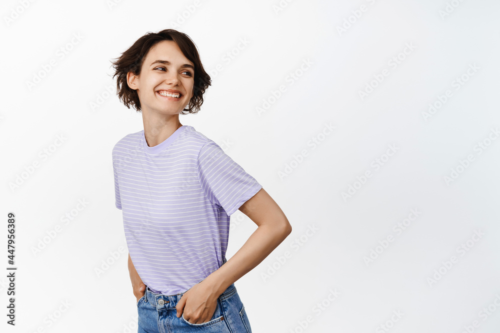 Carefree girl, posing against isolated white background, turn behind shoulder, laughing and smiling happy, hands in pockets, looking at empty copy space for your logo or sale banner Carefree girl, posing against isolated white background, turn behind shoulder, laughing and smiling happy, hands in pockets, looking at empty copy space for your logo or sale banner