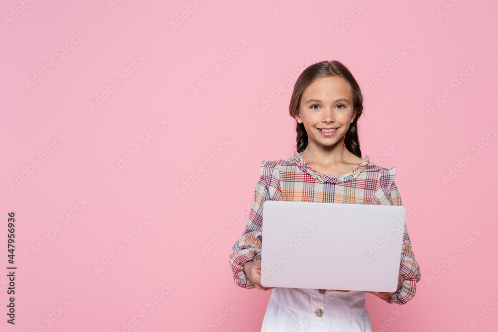 preteen girl smiling at camera while holding laptop isolated on pink preteen girl smiling at camera while holding laptop isolated on pink