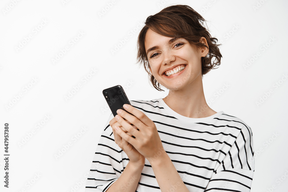 Beautiful brunette girl using smartphone cellular, holding mobile phone and smiling happy at camera. Technology concept