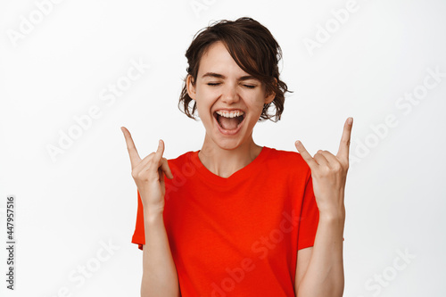 Happy modern girl partying, showing tongue and heavy metal horns, rock n roll gesture, smiling and enjoying the fun of concert, white background photo