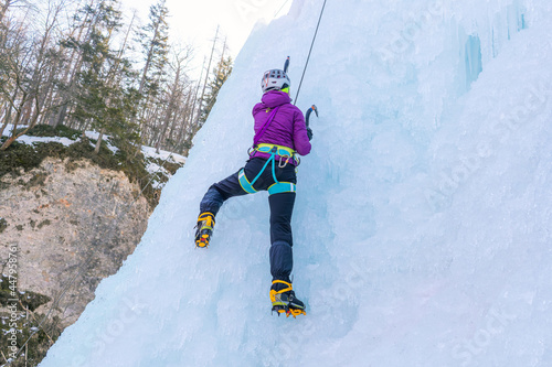 Female ice climber in traction position, swinging ice axes overhead and planting the pick in the ice, side view