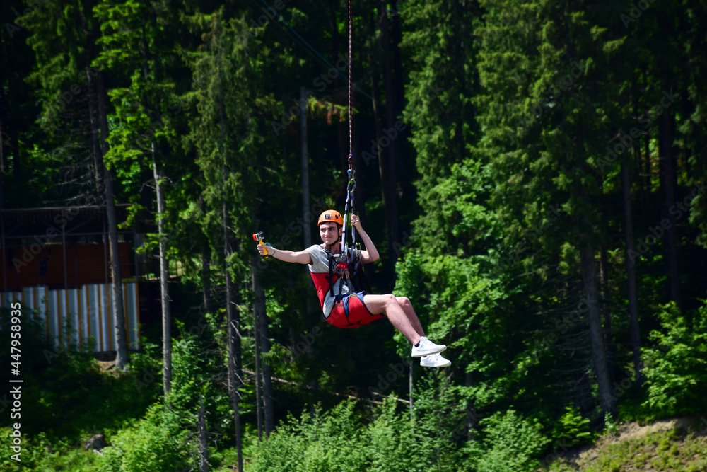 A young man jumped from bungee jumping and now hangs on a rope and films himself on a sports video camera against a blurred background of a green forest