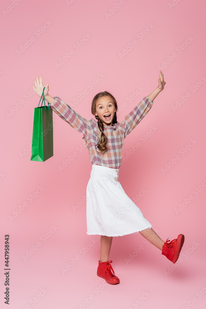 excited girl with green shopping bag raising hands on pink background excited girl with green shopping bag raising hands on pink background