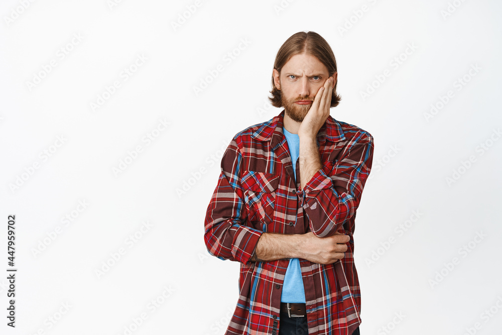 Grumpy and upset blond man, frowning displeased, lean head on hand, staring with angry annoyed face expression, bothered by smth, standing over white background Grumpy and upset blond man, frowning displeased, lean head on hand, staring with angry annoyed face expression, bothered by smth, standing over white background