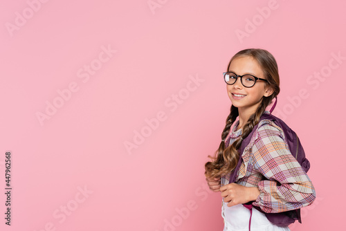 Quadro em tela Preteen schoolgirl in eyeglasses and backpack smiling at camera isolated on pink