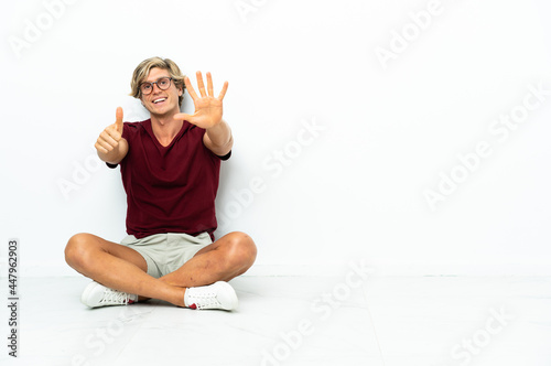 Young English man sitting on the floor counting six with fingers