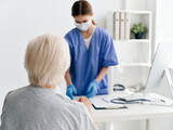 nurse with documents at the table in the office and an elderly patient in a medical mask covid passport