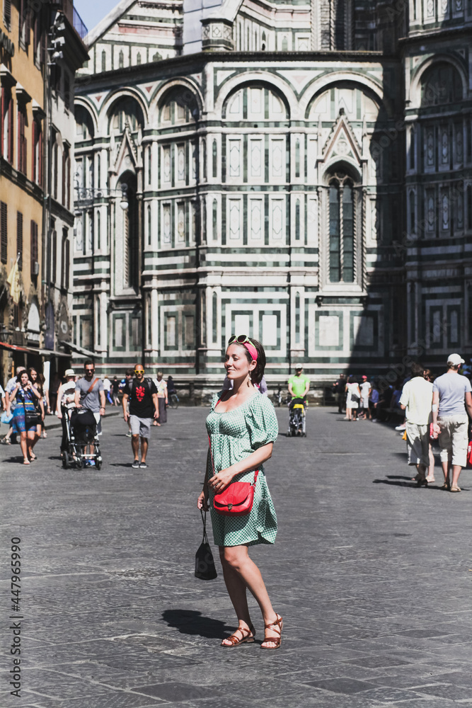 Young woman in a scarf and sunglasses with red bag on a sunny day posing for a photograph on the background of an Italian street, tourist, travel, frontal photography, full-length portrait