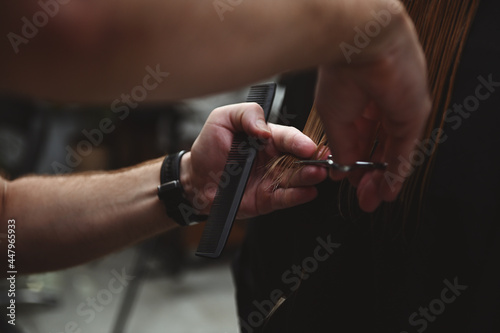 Close-up of hairdresser holding a hairdresser scissors and a comb and cutting woman's hair at beauty salon