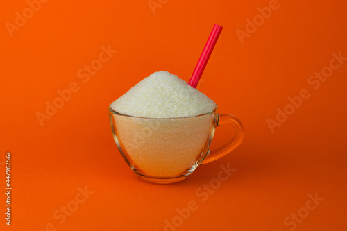Granulated sugar in a cup with a cocktail tube on an orange background