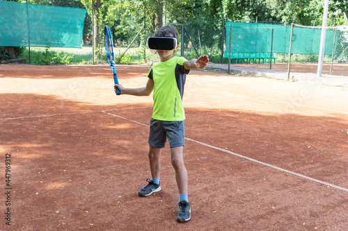 Online tennis training of boy in VR glasses standing on tennis court and preparing to make kick. New reality in sport, training in cyberspace. © Anna