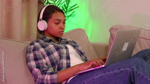 Tired young woman lying on the couch with a laptop listening to music. Grueling work. He listens to music with big white headphones. The concept of working online and freelancing.