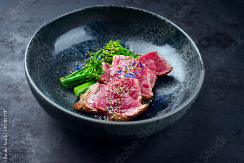 Modern style baby broccoli with fried dry aged sliced beef fillet steak served as close-up on a Nordic design plate