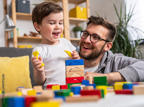 Young happy family. Mother and father playing with her cute toddler son at home using didactic wooden toys. Home education