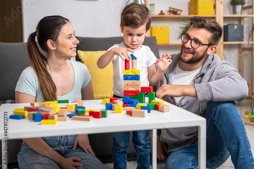 Young happy family. Mother and father playing with her cute toddler son at home using didactic wooden toys. Home education