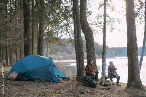 Family couple is resting on the shore of the lake with a tent. Fashing camp with a fire in the forest.