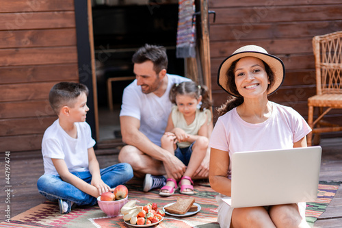 Freelance woman working with laptop, sitting on porch during family vacation, enjoying wifi and 5g and enjoying the opportunity to work remotely from the office 