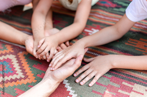 Adults and children holding hands lying on a colored red embroidered carpet, the family relaxing together in their friendly circle