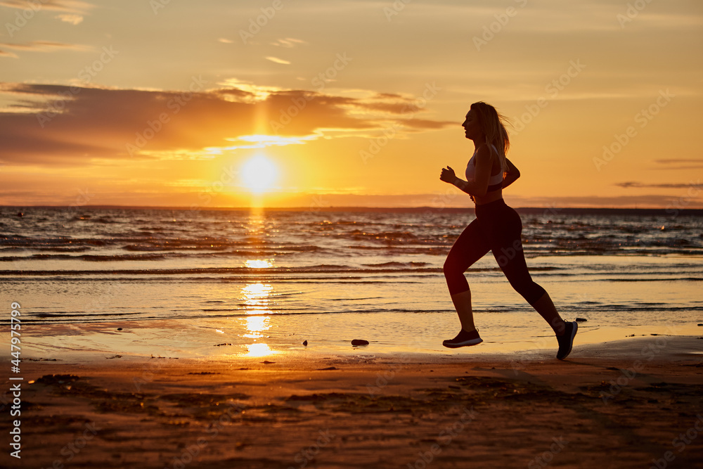 Healthy woman runs outdoors during sunset near shore.