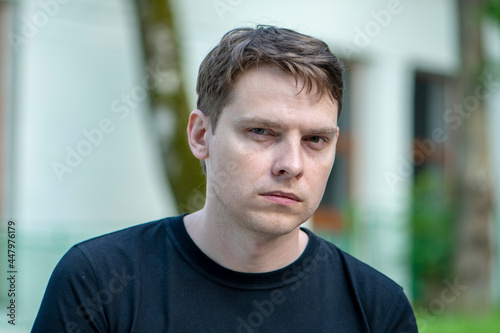 Portrait of a 35-40-year-old man in a black T-shirt on a blurry urban background. Perhaps he is an IT specialist, a specialist in travel, a buyer from a store, a recipient.