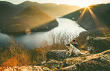 man and his dog sitting on rock enjoying amazing autumn view over lake at sunset