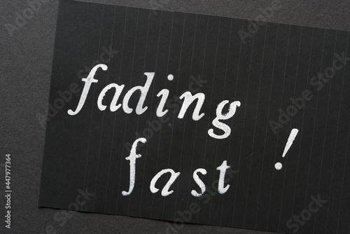 the words "fading fast" loosely stencilled on black notepad paper and arranged on a dark gray paper background 