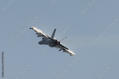 U.S. Navy EA-18G Growler in a high G maneuver, with afterburners on and condensation clouds over the wings