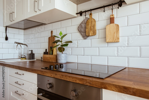 Kitchen brass utensils, chef accessories. Hanging kitchen with white tiles wall and wood tabletop.Green plant on kitchen background