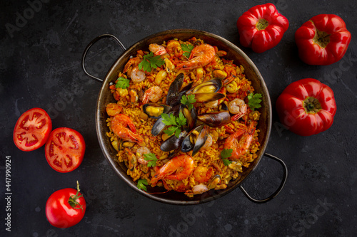 Traditional spanish seafood paella with rice, mussels, shrimps in a pan with tomatoes on dark background. view from above, flat lay