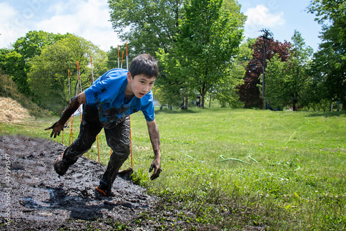 Φωτογραφία Young boy covered in mud running through fun muddy outdoor obstacle course in a field