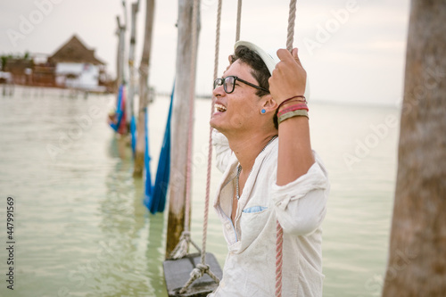 young man smiles on swings in the sea