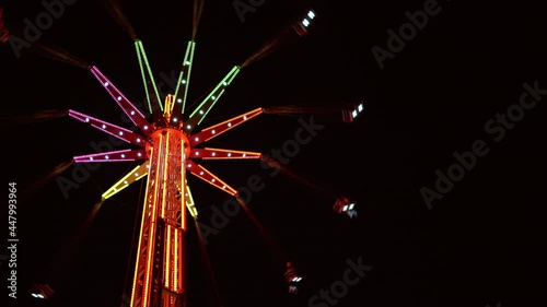 4K multicoloured illuminated tall merry-go-round rotating in night sky. Entertainment, amusement park concept. photo
