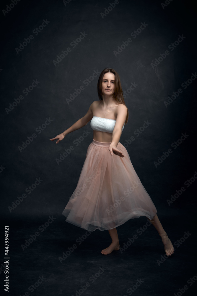 Young girl in white top and peach skirt dancing in black old textured studio