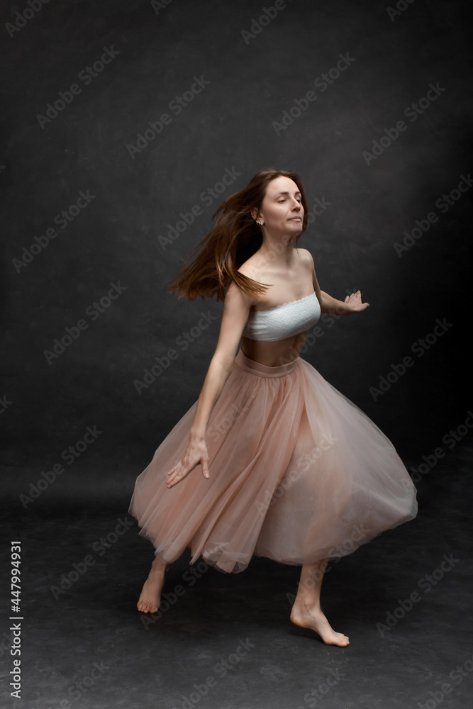 Young girl in white top and peach skirt dancing in black old textured studio Young girl in white top and peach skirt dancing in black old textured studio