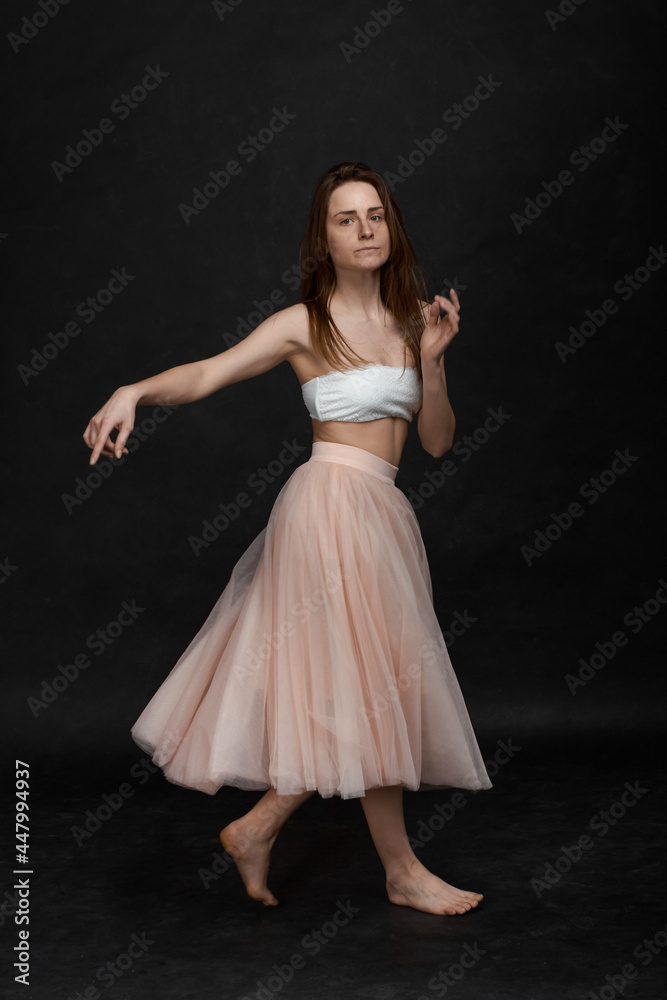 Naklejka premium Young girl in white top and peach skirt dancing in black old textured studio