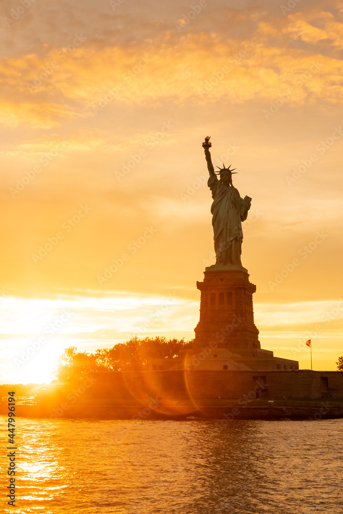 The Statue of Liberty at New York city during sunset with reflections on the ocean