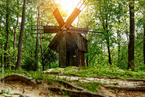 An ancient mill in the forest is illuminated by the rays of the sun.