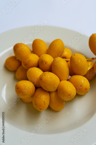 Yellow raw of date palm fresh with water droplets,undried date fruit sweet healthy fruits in white plate and  isolated on white background. photo