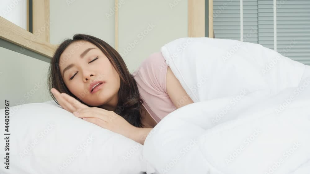 Asian beautiful woman waking up in the morning at home. Young girl stretches and gets up from bed in bedroom at home. Concept of lifestyle, vacation and healthy. Asian beautiful woman waking up in the morning at home. Young girl stretches and gets up from bed in bedroom at home. Concept of lifestyle, vacation and healthy.